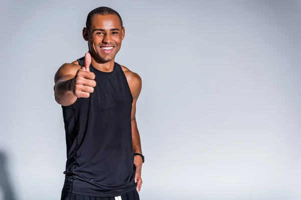 Alegre Africano americano desportista mostrando polegar para cima e sorrindo para a câmera isolada em cinza — Fotografia de Stock