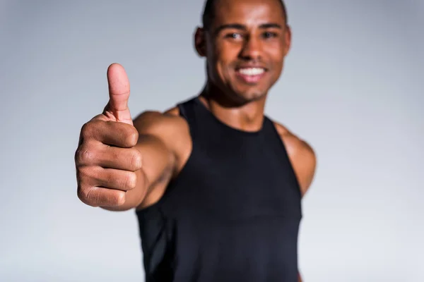 Крупный план улыбающегося африканского спортсмена, показывающего большой палец, изолированный на сером — стоковое фото