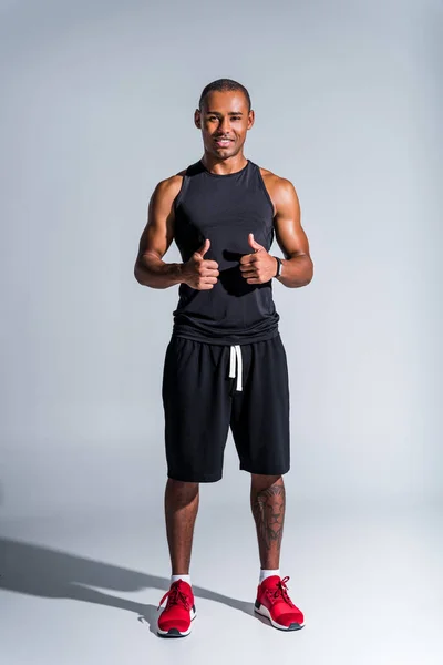 Cheerful african american sportsman showing thumbs up and smiling at camera isolated on grey — Stock Photo