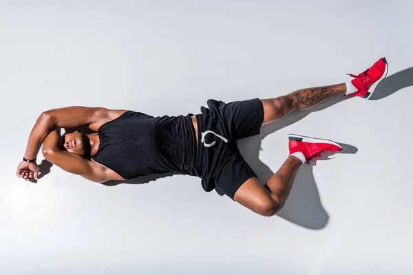 Vue de dessus du jeune homme afro-américain aux yeux fermés portant des vêtements de sport et couché sur le gris — Photo de stock