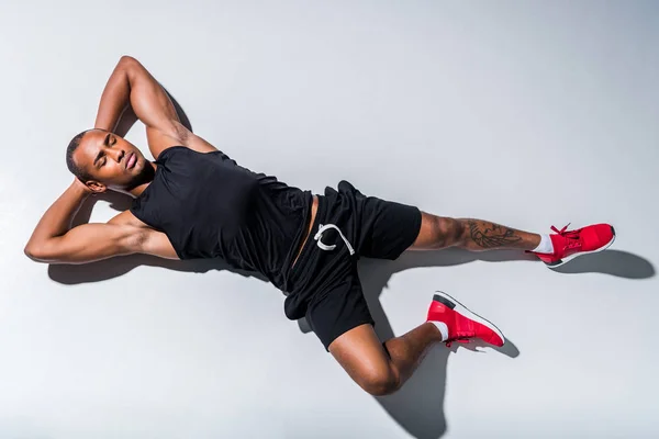 Vista dall'alto del giovane sportivo afroamericano con gli occhi chiusi sdraiato sul grigio — Foto stock