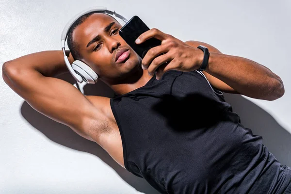 Joven afroamericano hombre en auriculares con teléfono inteligente en gris — Stock Photo