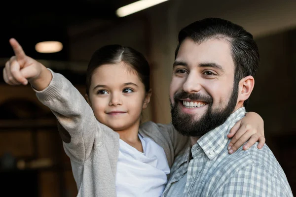 Fröhliche Tochter umarmt Vater und zeigt auf etwas zu Hause — Stockfoto