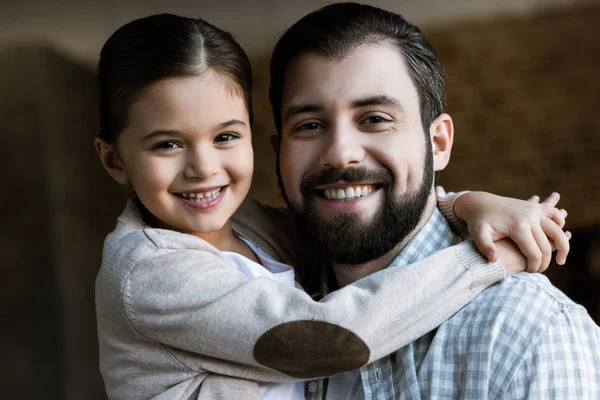 Fröhlicher Vater und Tochter, die sich umarmen und zu Hause in die Kamera schauen — Stockfoto