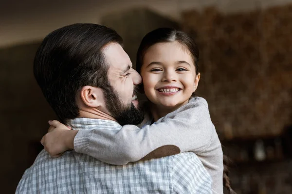 Fröhlicher Vater und Tochter, die sich umarmen und zu Hause in die Kamera schauen — Stockfoto