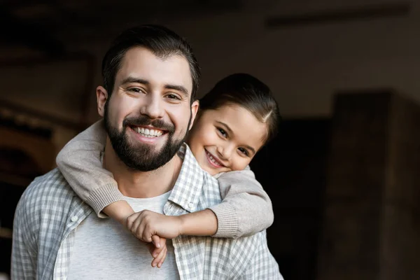 Fröhlicher Vater und Tochter, die sich umarmen und zu Hause in die Kamera schauen — Stockfoto