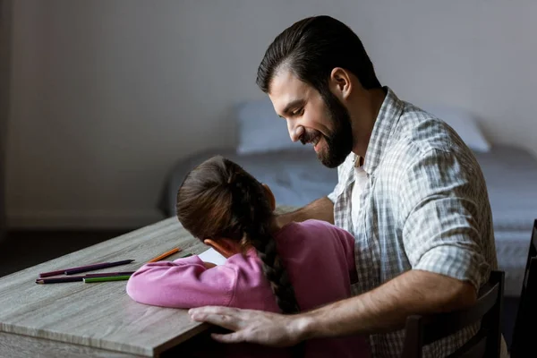 Вид збоку батька з маленькою донькою, що сидить за столом і малює в скрапбуці вдома — стокове фото