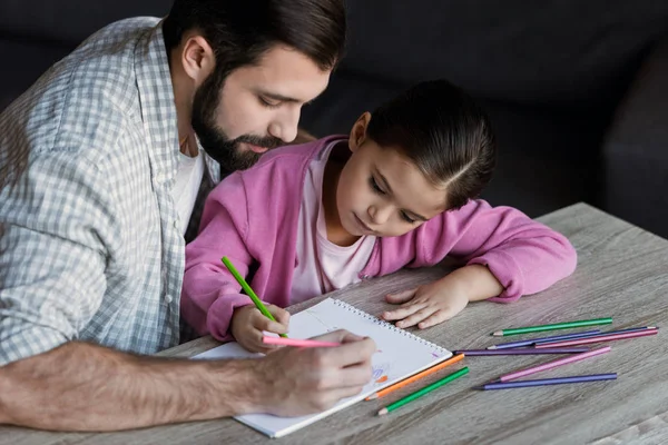 Padre con figlioletta seduta a tavola e disegno in album a casa — Foto stock