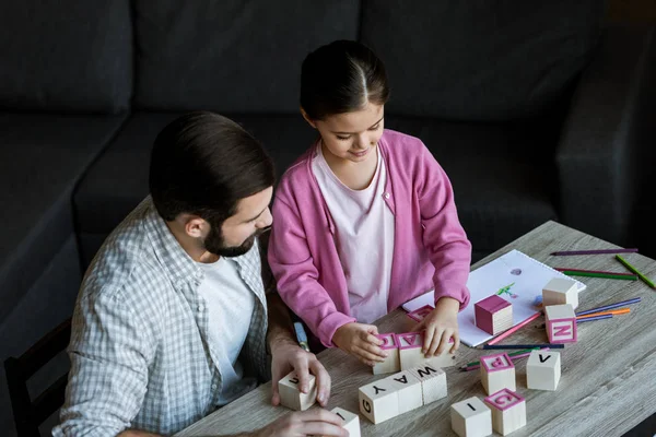 Отец с дочерью сидят за столом и делают слова кубиками с письмами на дому — Stock Photo