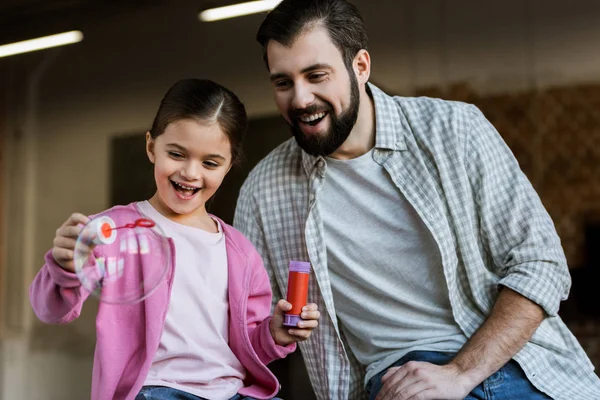 Happy father with daughter blowing bubbles at home — Stock Photo