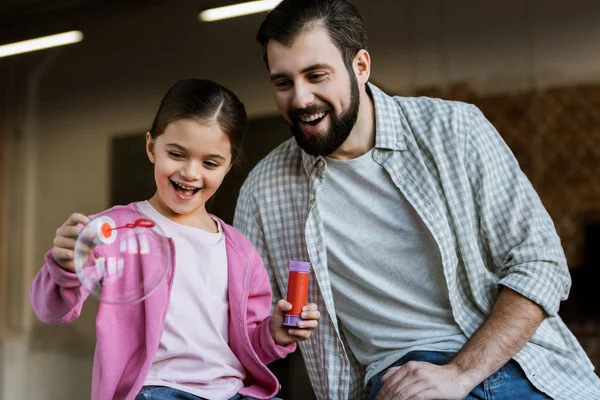 Pai feliz com a filha soprando bolhas em casa — Fotografia de Stock