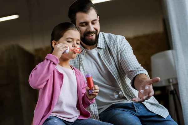 Felice padre con figlia che soffia bolle a casa — Foto stock