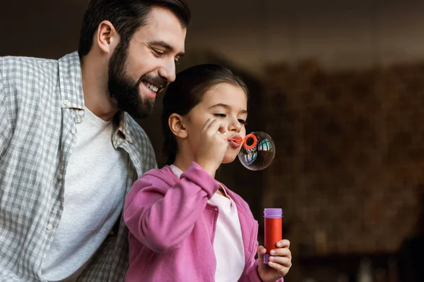 Heureux père avec fille soufflant des bulles à la maison — Photo de stock