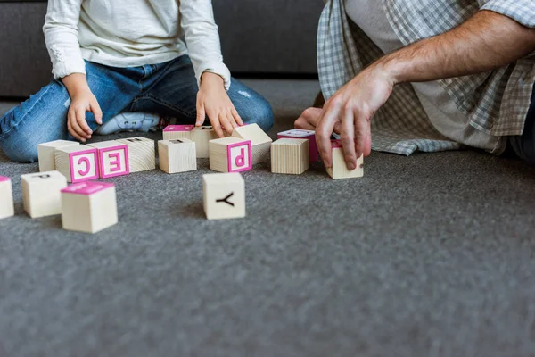 Обрізане зображення батька з дочкою робить слова кубиками з літерами вдома — стокове фото
