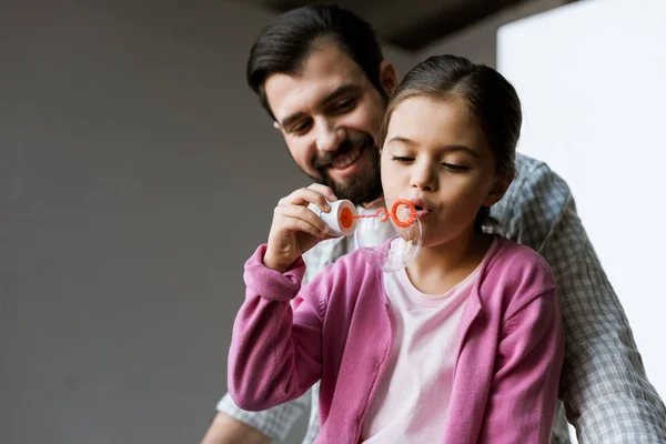 Happy father with daughter blowing bubbles at home — Stock Photo