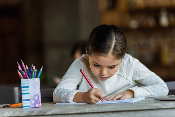 Petit enfant assis à table et dessin dans scrapbook à la maison — Photo de stock