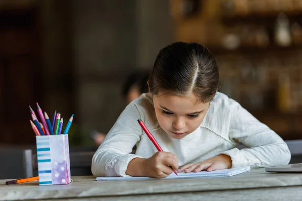 Kleines Kind sitzt am Tisch und zeichnet zu Hause in Sammelalbum — Stockfoto