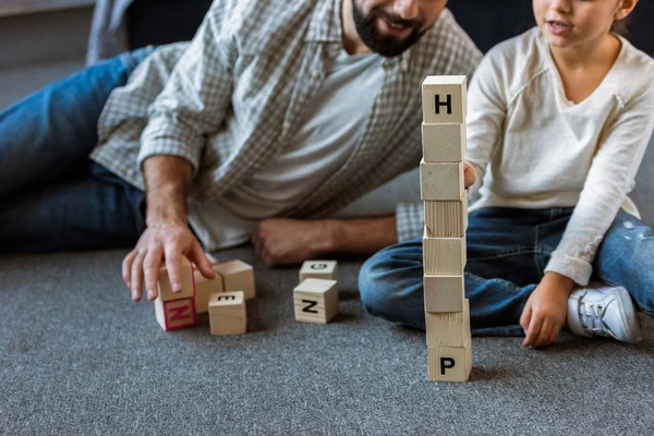 Imagen recortada de padre con hija haciendo palabras por cubos con letras en casa - foto de stock