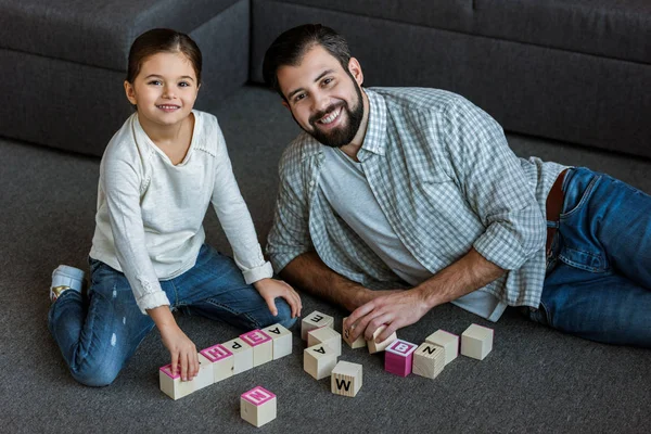 Padre allegro con figlia che fa parole da cubi con lettere a casa — Foto stock