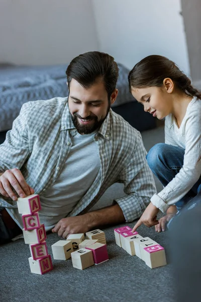 Alegre padre con hija haciendo palabras por cubos con letras en casa - foto de stock