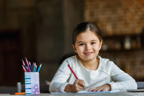 Bambino piccolo seduto a tavola e disegno in scrapbook a casa — Foto stock