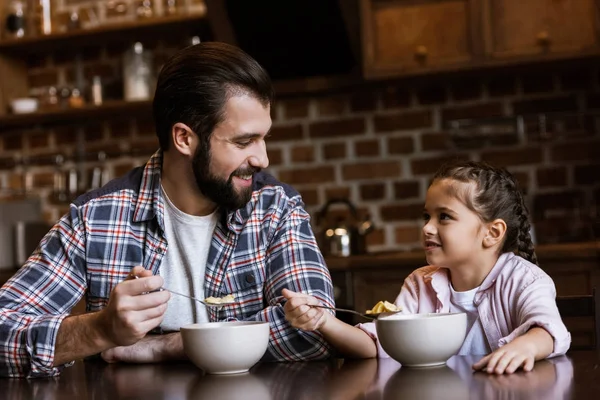 Joyeux père et fille assis à table et manger des collations avec du lait à la cuisine — Photo de stock