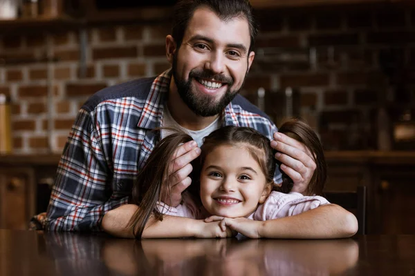Happy father with daughter sitting at table and looking at camera at home — Stock Photo