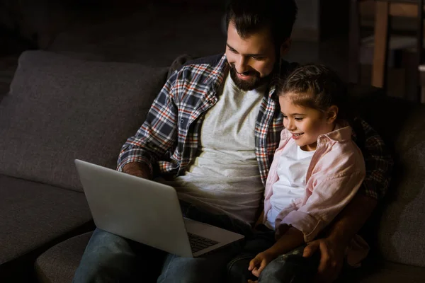 Pai alegre com a filha sentada no sofá e usando laptop — Fotografia de Stock