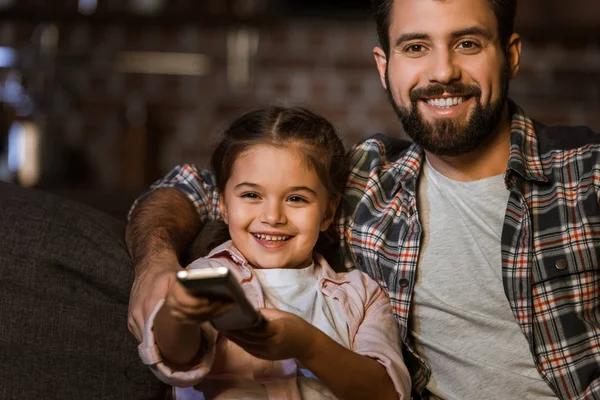 Glücklicher Vater mit Tochter, die auf der Couch sitzt, sich umarmt und zu Hause fernsieht — Stockfoto