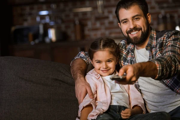 Happy father with daughter sitting in couch, hugging and watching TV at home — Stock Photo