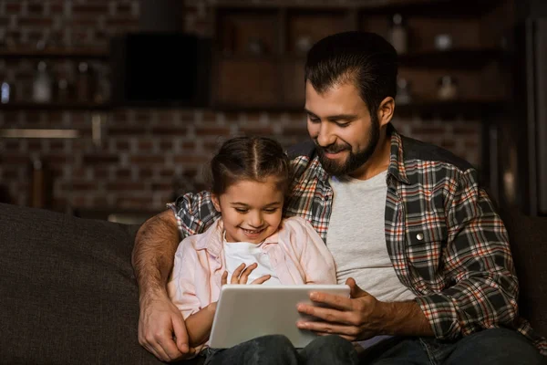 Pai feliz com a filha sentada no sofá e usando tablet — Fotografia de Stock