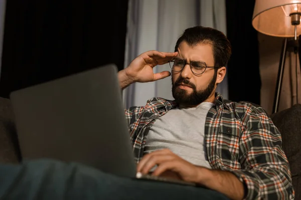 Tired man in glasses sitting on couch with laptop — Stock Photo