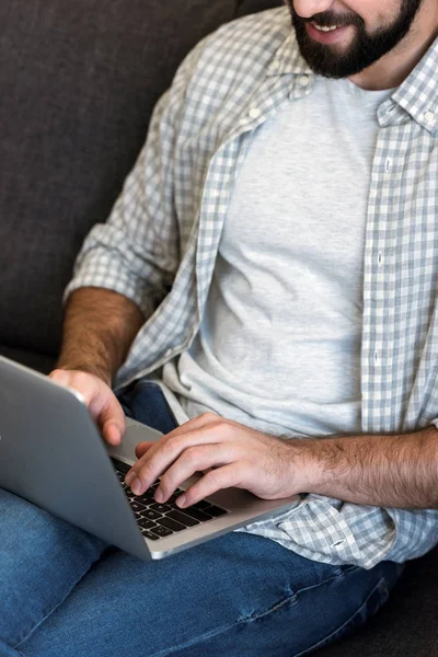 Cropped image of man sitting on couch and using laptop — Stock Photo