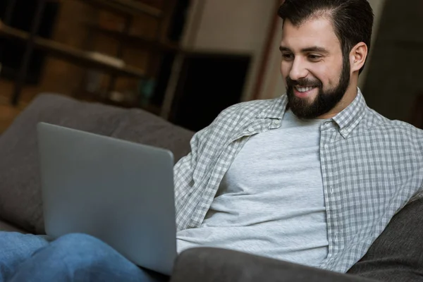 Schöner Mann sitzt auf Couch und benutzt Laptop — Stockfoto