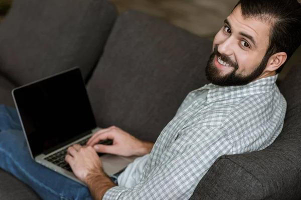 Bel homme assis sur le canapé et utilisant un ordinateur portable — Photo de stock