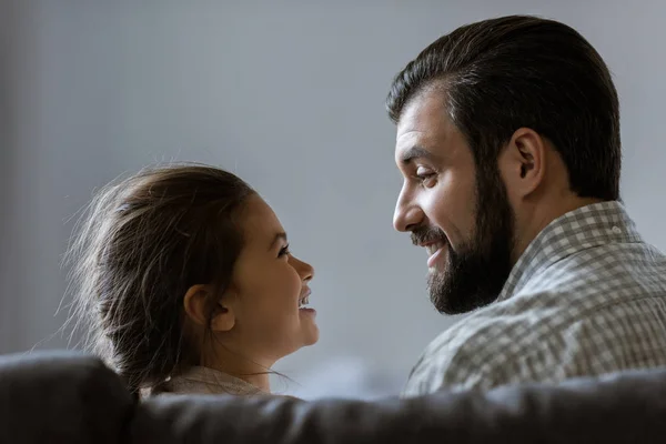 Padre feliz con la hija sonriendo y mirándose el uno al otro, vista trasera - foto de stock