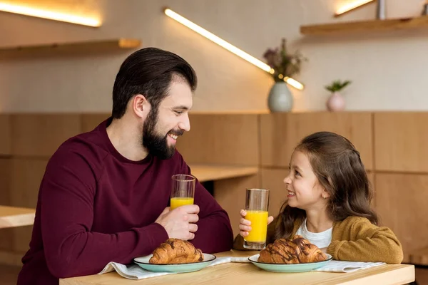 Glücklicher Vater und Tochter halten Gläser mit Orangensaft in der Hand und schauen einander an — Stockfoto
