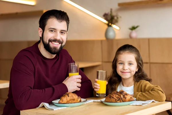 Sonrientes padre e hija sosteniendo vasos con jugo y mirando a la cámara - foto de stock