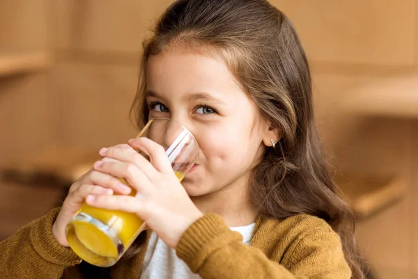 Criança adorável bebendo suco de laranja no café e olhando para a câmera — Fotografia de Stock