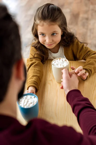 Над головой вид счастливой дочери и отца меняя их чашки какао с зефиром — стоковое фото