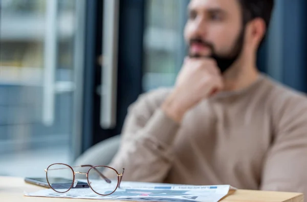 Homme réfléchi assis dans un café avec des lunettes au premier plan — Photo de stock