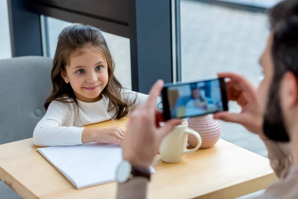 Cropped image of father taking photo of smiling daughter in cafe — Stock Photo