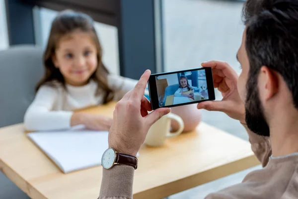 Cropped image of father taking photo of daughter in cafe — Stock Photo