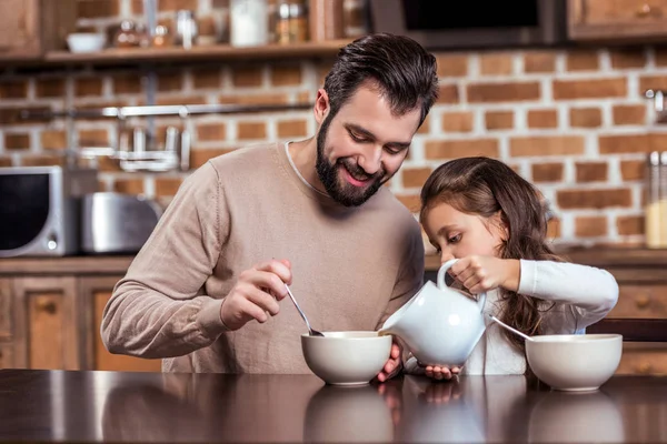 Tochter schüttet Milch in Küche auf Teller des Vaters — Stockfoto
