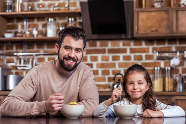 Sonrientes padre e hija desayunando y mirando a la cámara - foto de stock