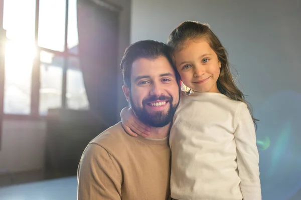 Sonrientes padre e hija posando en la habitación y mirando a la cámara - foto de stock