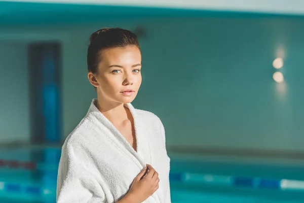 Belle jeune femme en peignoir devant la piscine au spa — Photo de stock