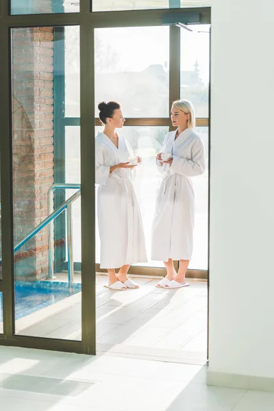 Beautiful young women in bathrobes drinking coffee at spa center — Stock Photo