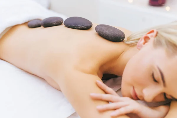 Primer plano de la mujer joven recibiendo terapia de piedra en el salón de spa - foto de stock