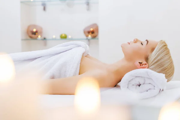 Attractive young woman relaxing on massage table at spa salon — Stock Photo